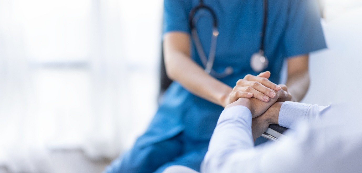 Patient and healthcare provider holding hands in hospital setting.